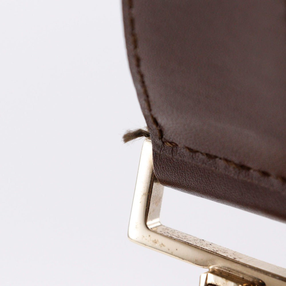 Close-up of a brown leather product with a gold buckle on a light gray background