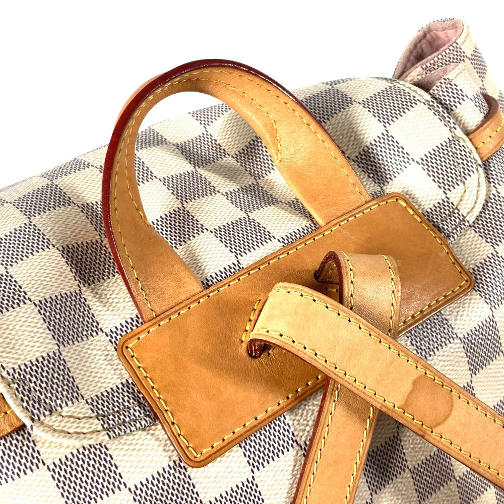 Close-up of a checkered bag with a brown leather handle and tag.
