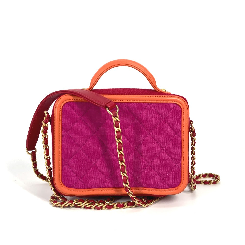 Pink quilted handbag with orange accents and gold chain strap on a white background