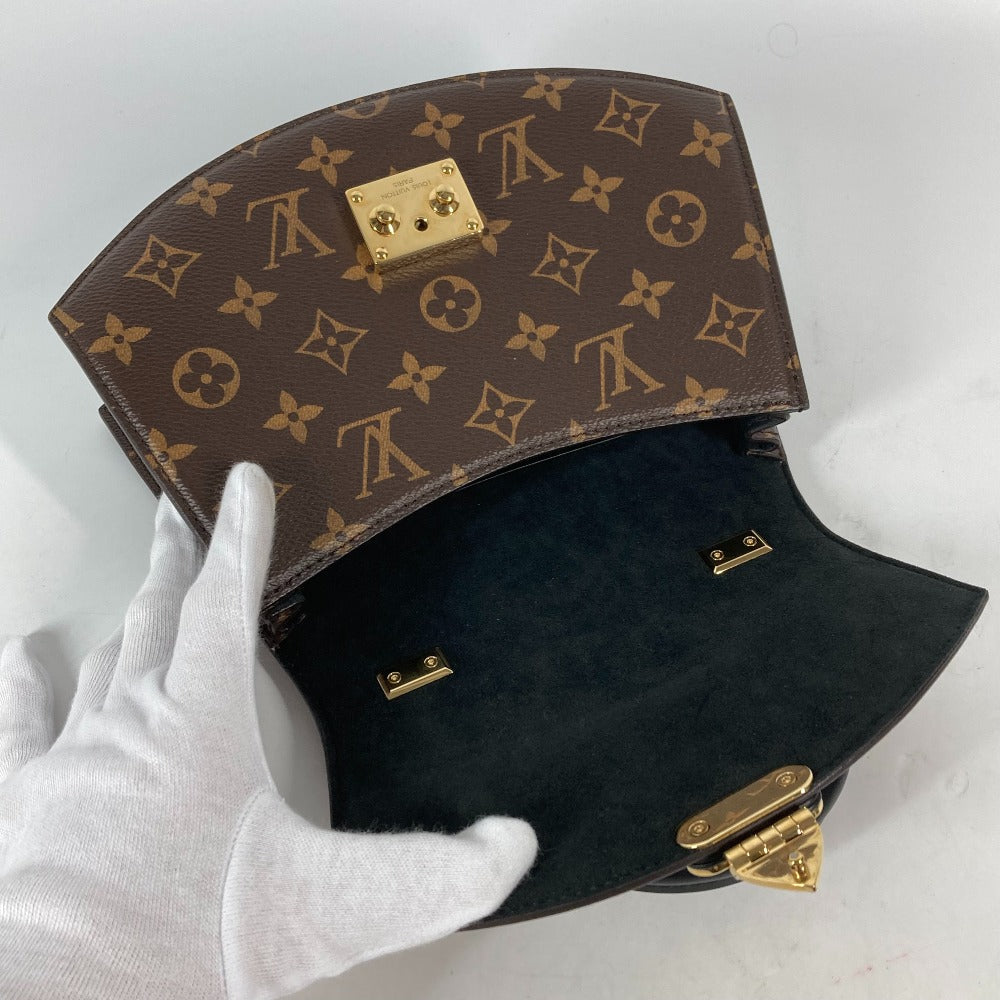 Designer handbag with monogram pattern held by a gloved hand on a light gray background