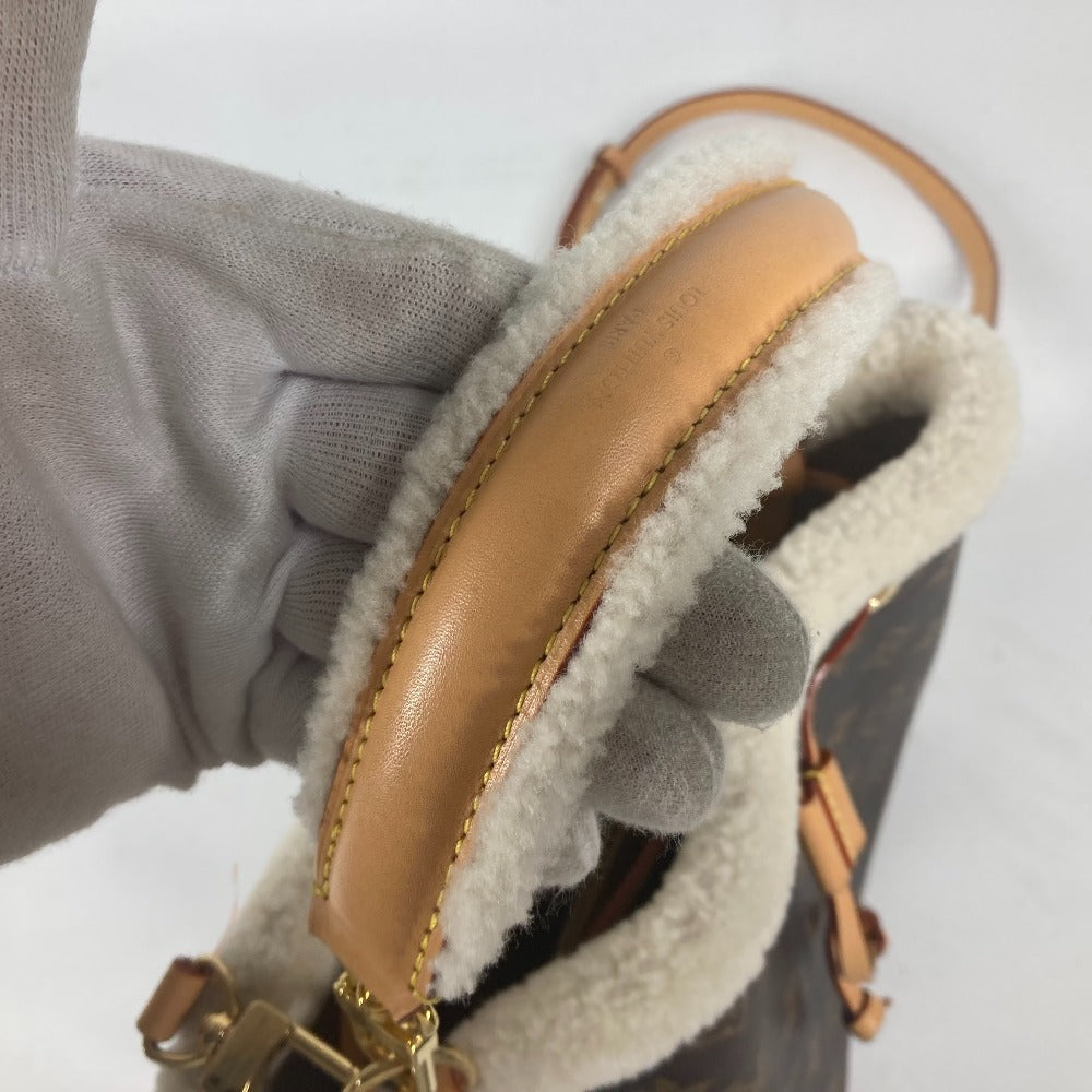Close-up of a brown leather bag with gold chain detail held by a gray glove.