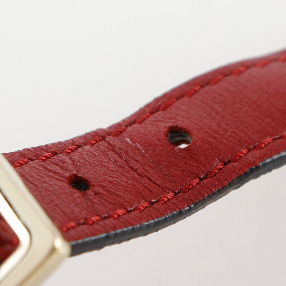 Close-up of a red leather watch strap with gold buckle on a light gray background