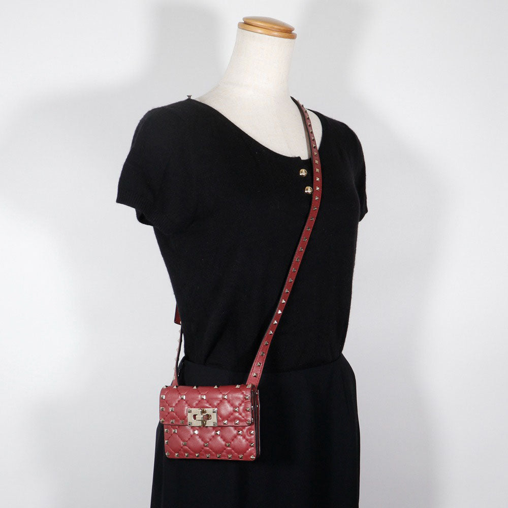 Black dress with a red quilted handbag on a mannequin against a white background