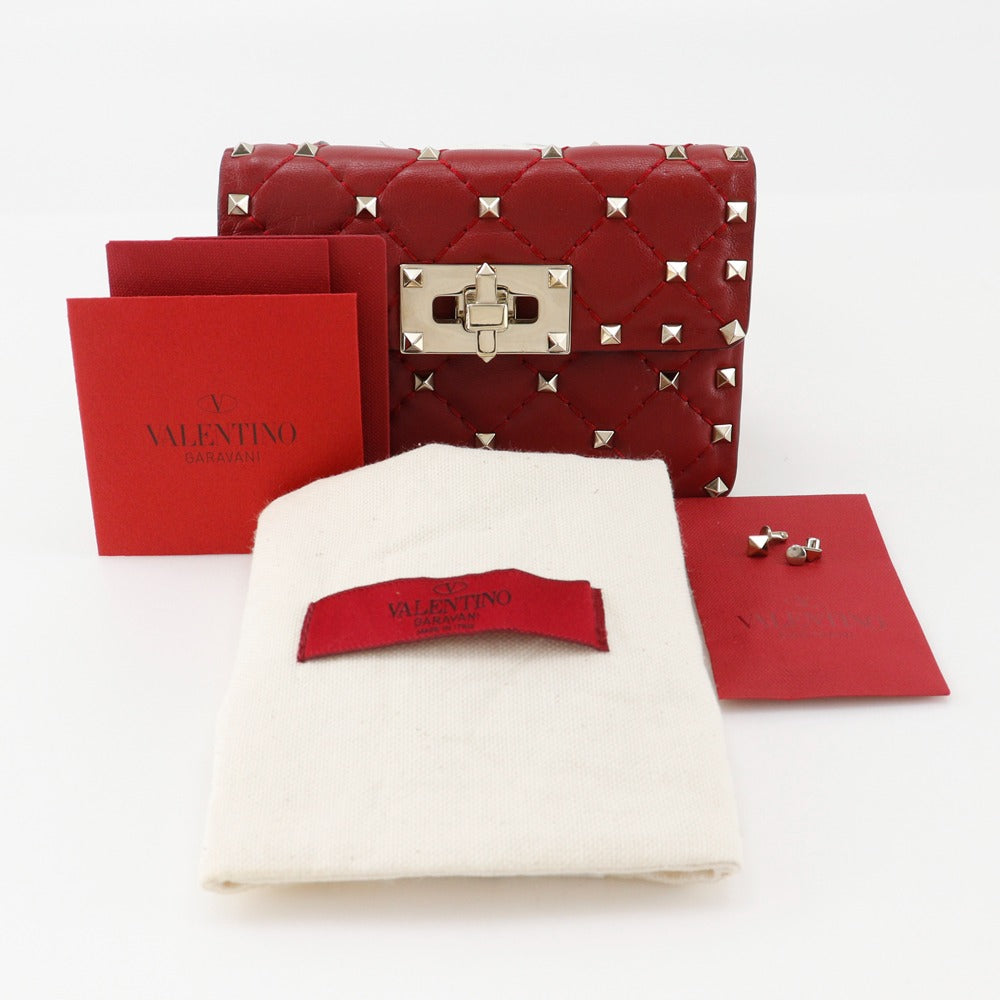 Red studded handbag with accessories on a white background