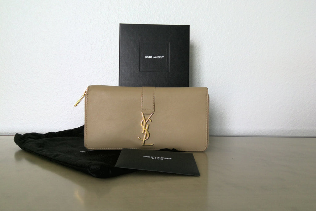Beige handbag with YSL logo next to a black Saint Laurent box on a light surface.