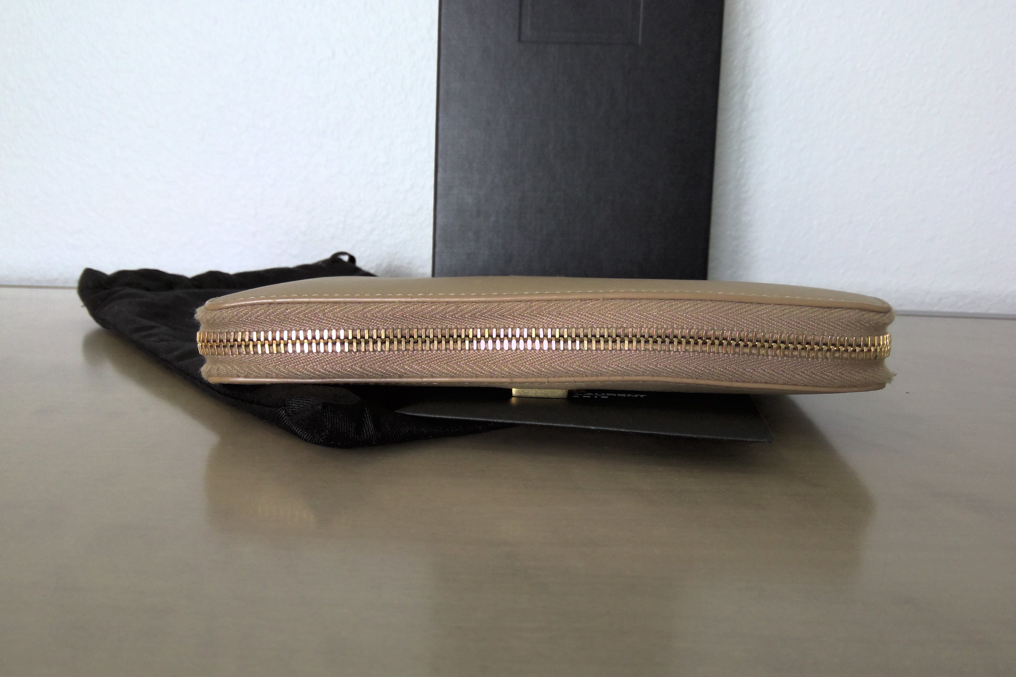 Beige zippered pouch with gold zipper on a reflective surface