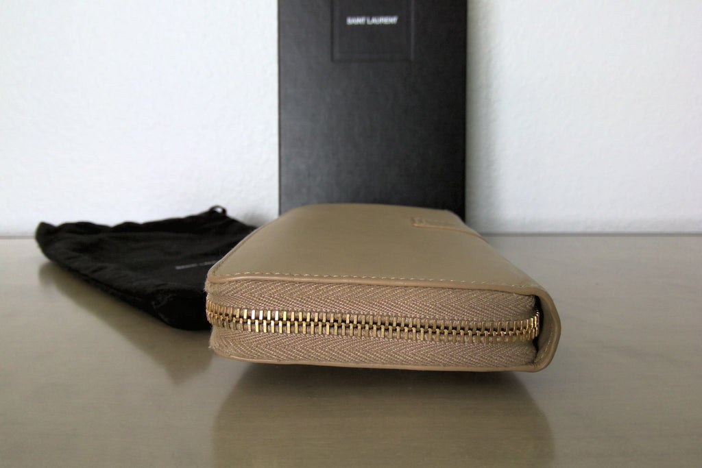 Brown leather wallet with gold zipper on a reflective surface, with a black leather item in the background.