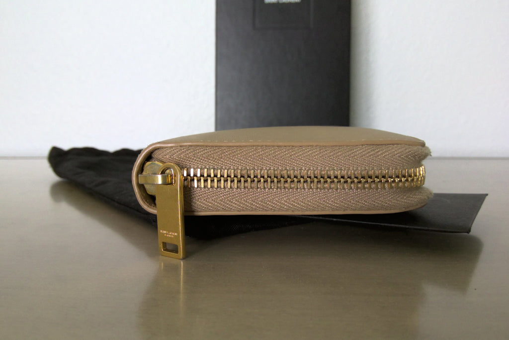 Beige zippered pouch with gold zipper on a reflective surface