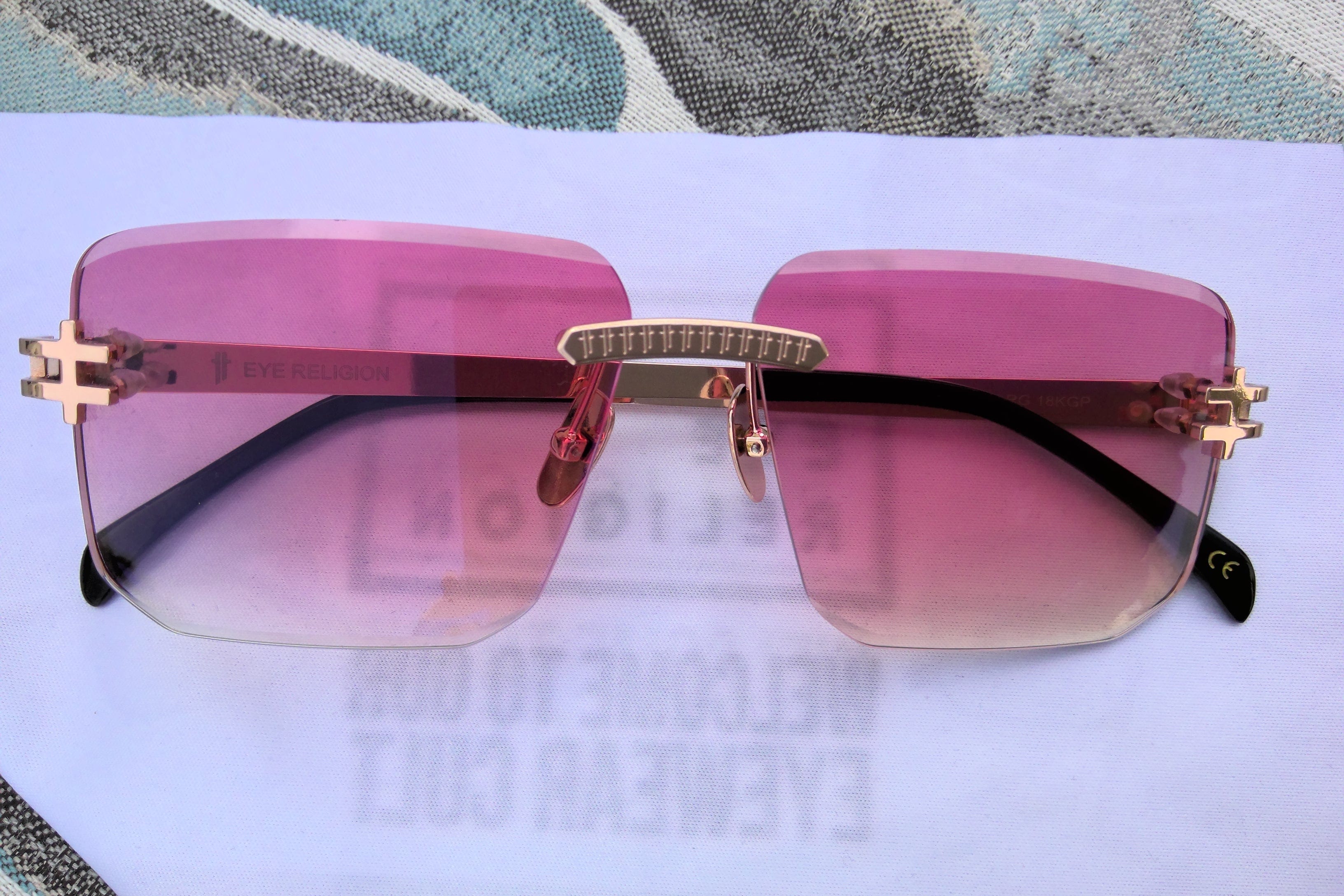 Sunglasses with pink lenses and gold frame on a white surface
