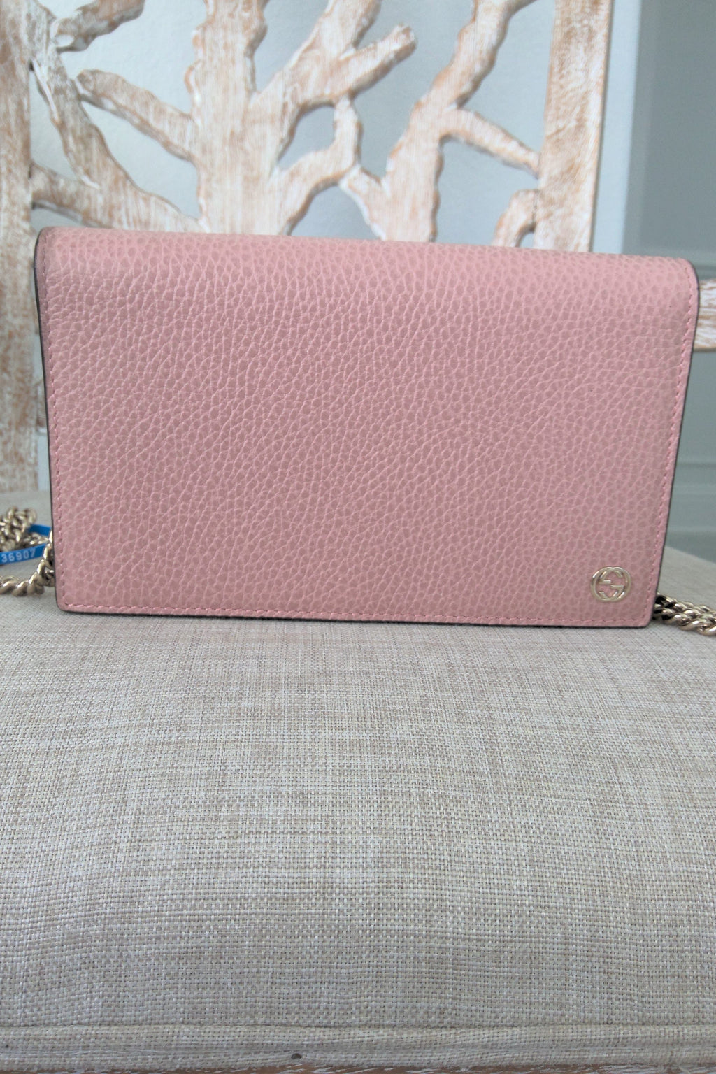 Pink textured handbag on a gray surface with a light blue wall and decorative branches in the background