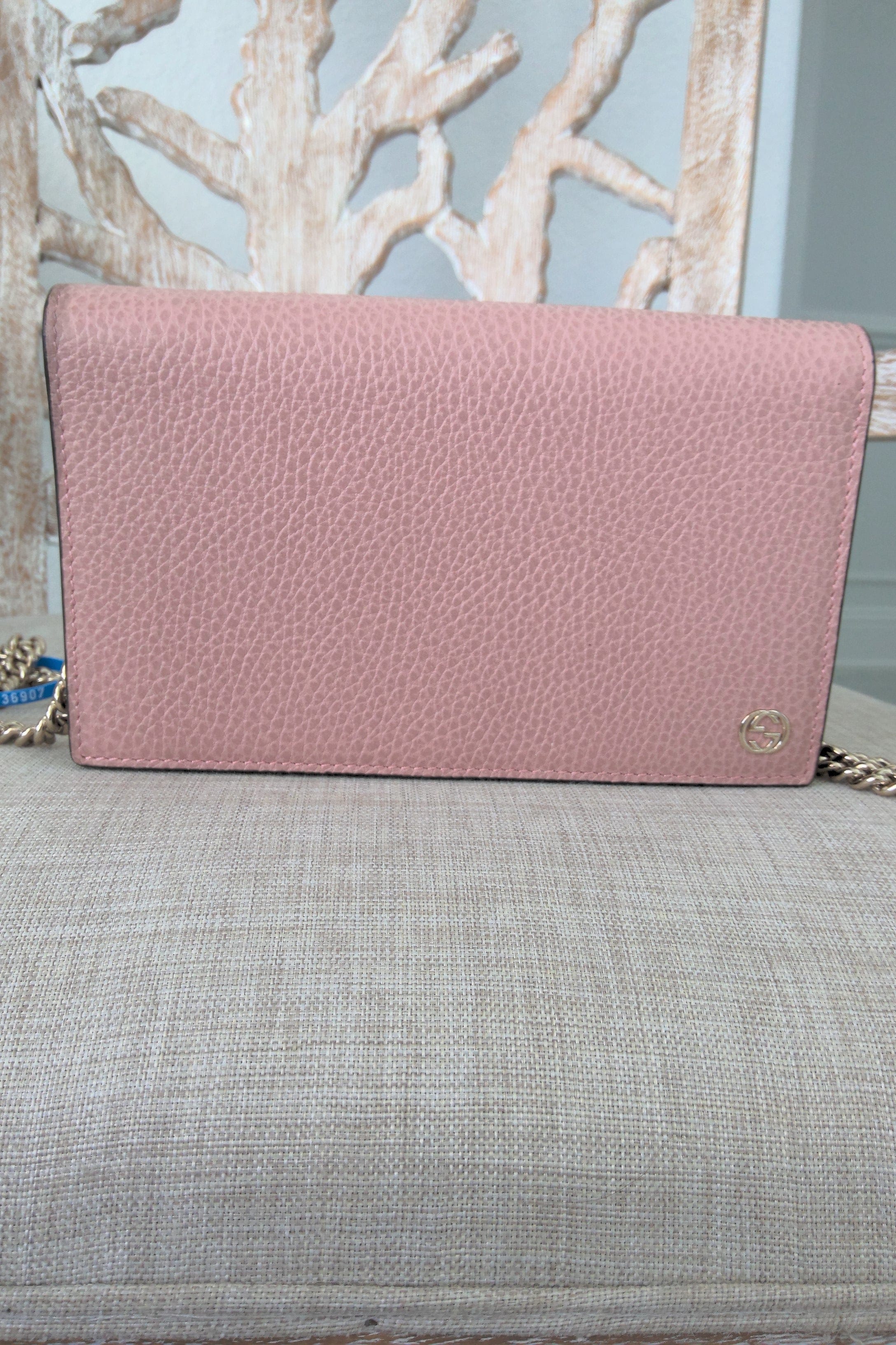 Pink textured handbag on a gray surface with a light blue wall and decorative branches in the background
