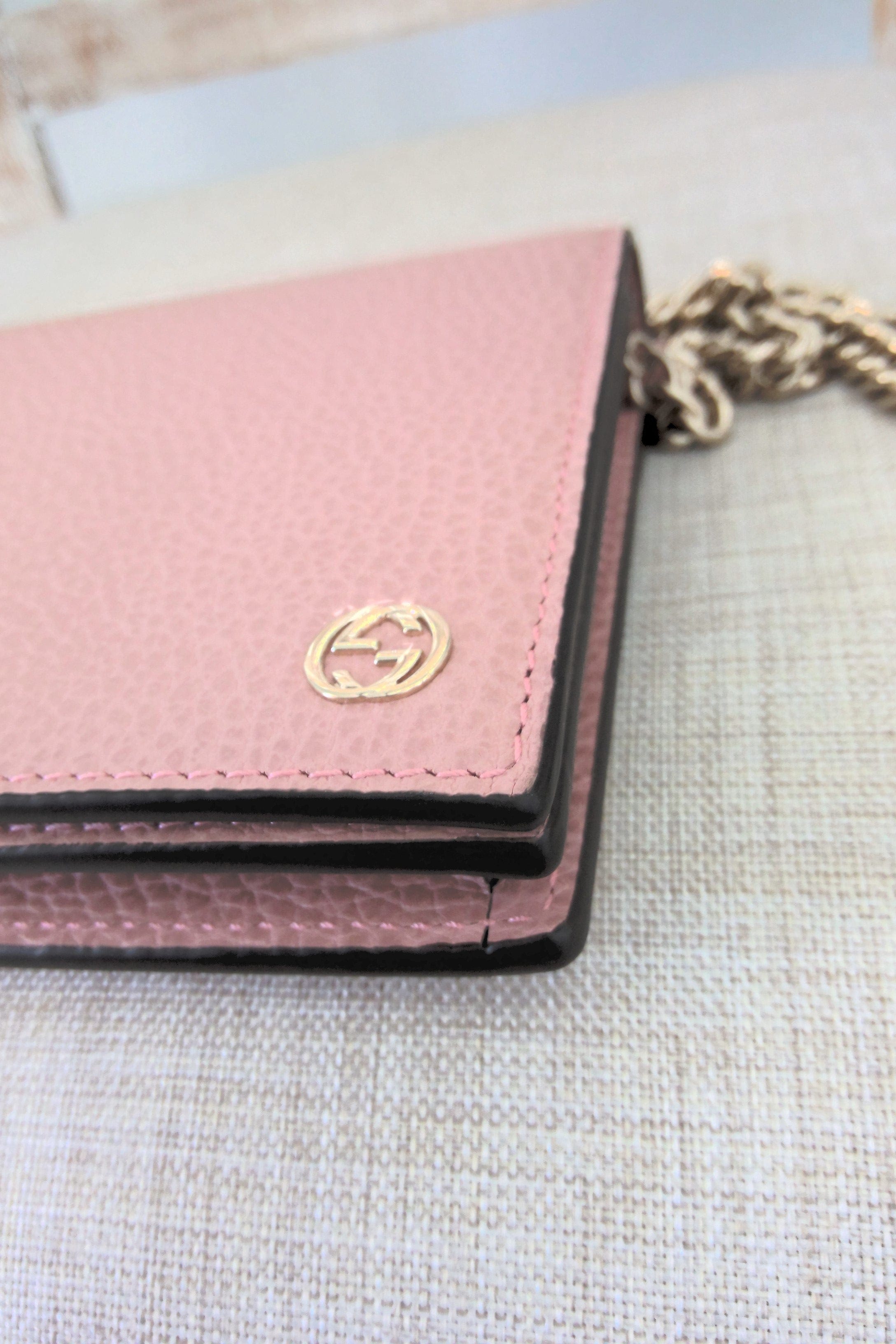 Pink wallet with gold logo on a textured surface