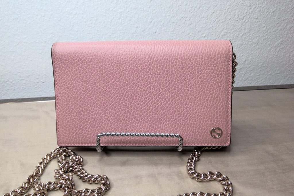 Pink handbag with a chain strap on a light gray surface.