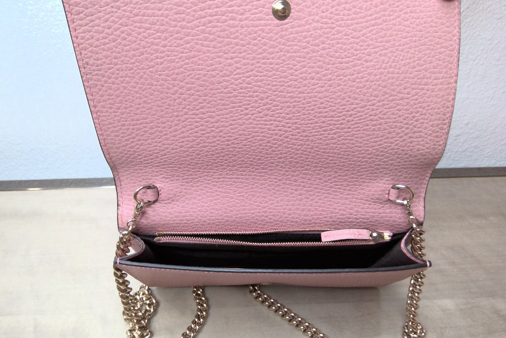 Pink handbag with chain strap on a light gray surface