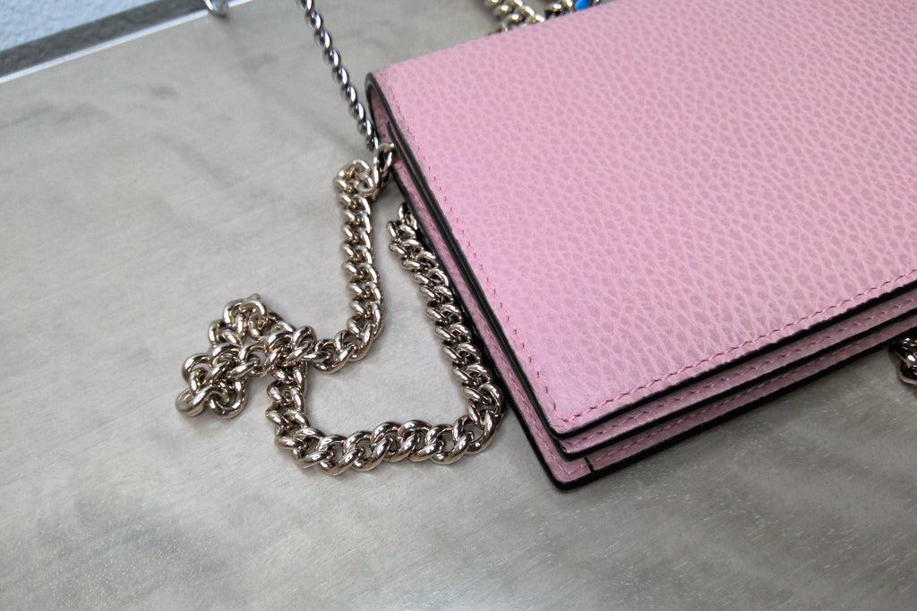 Pink wallet with a chain strap on a gray surface