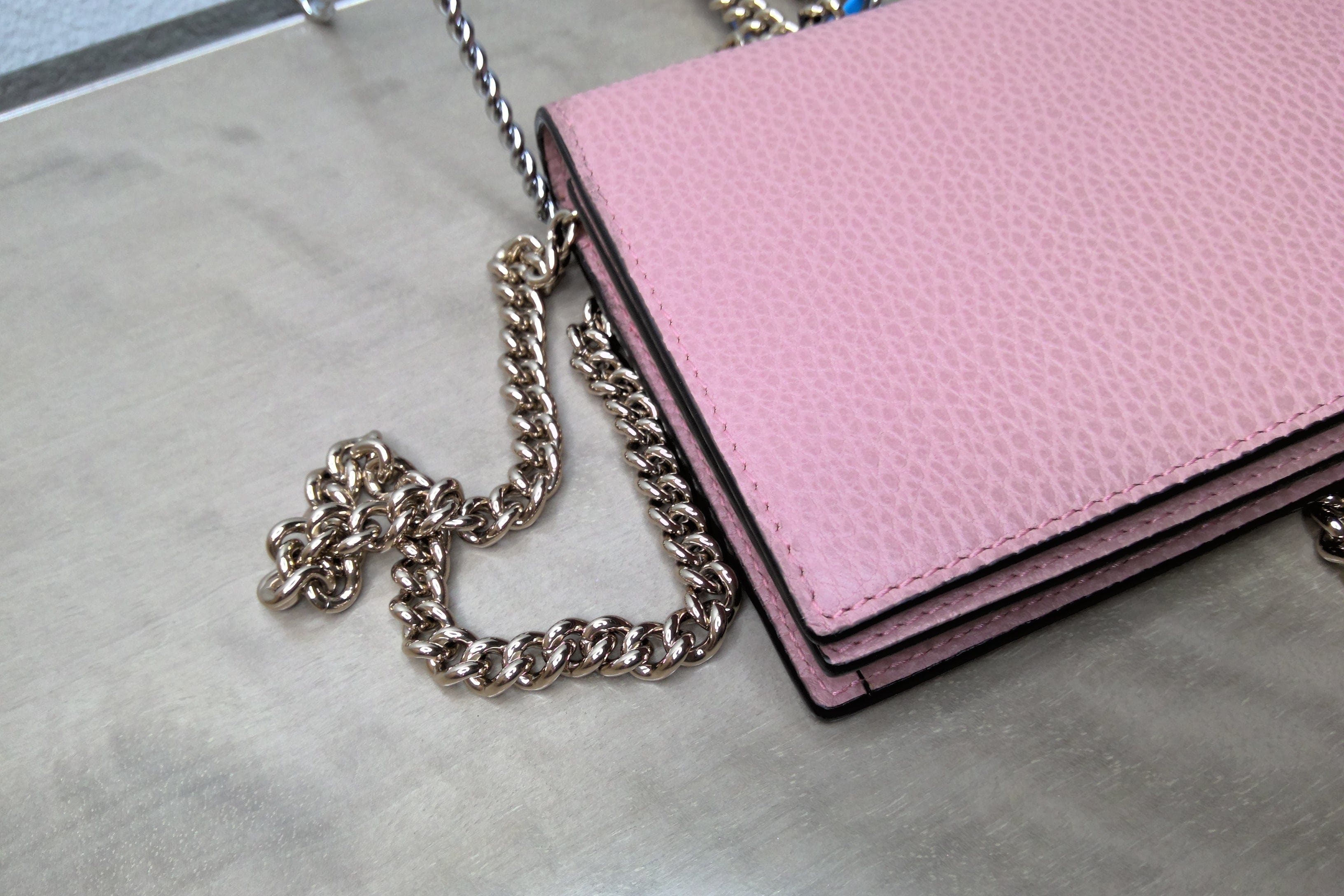 Pink wallet with a chain strap on a gray surface