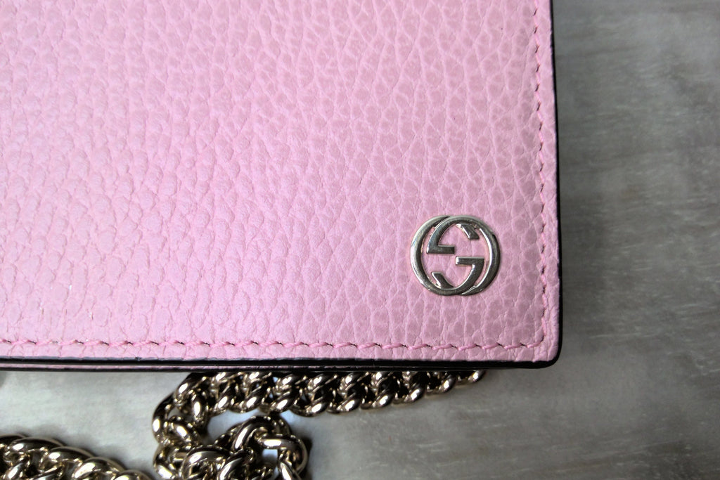 Pink wallet with a chain detail on a gray surface