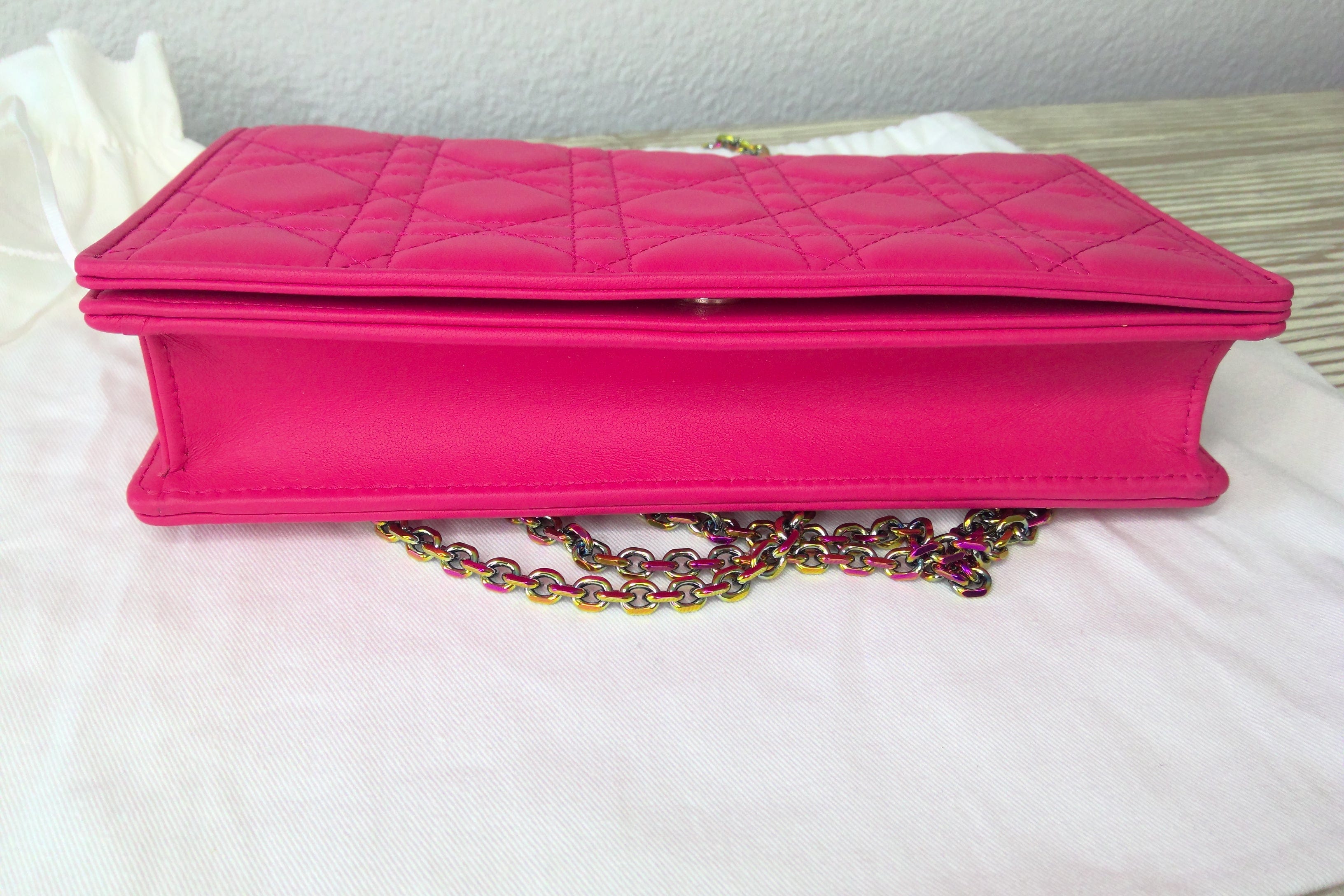 Pink quilted handbag with a colorful chain on a white surface