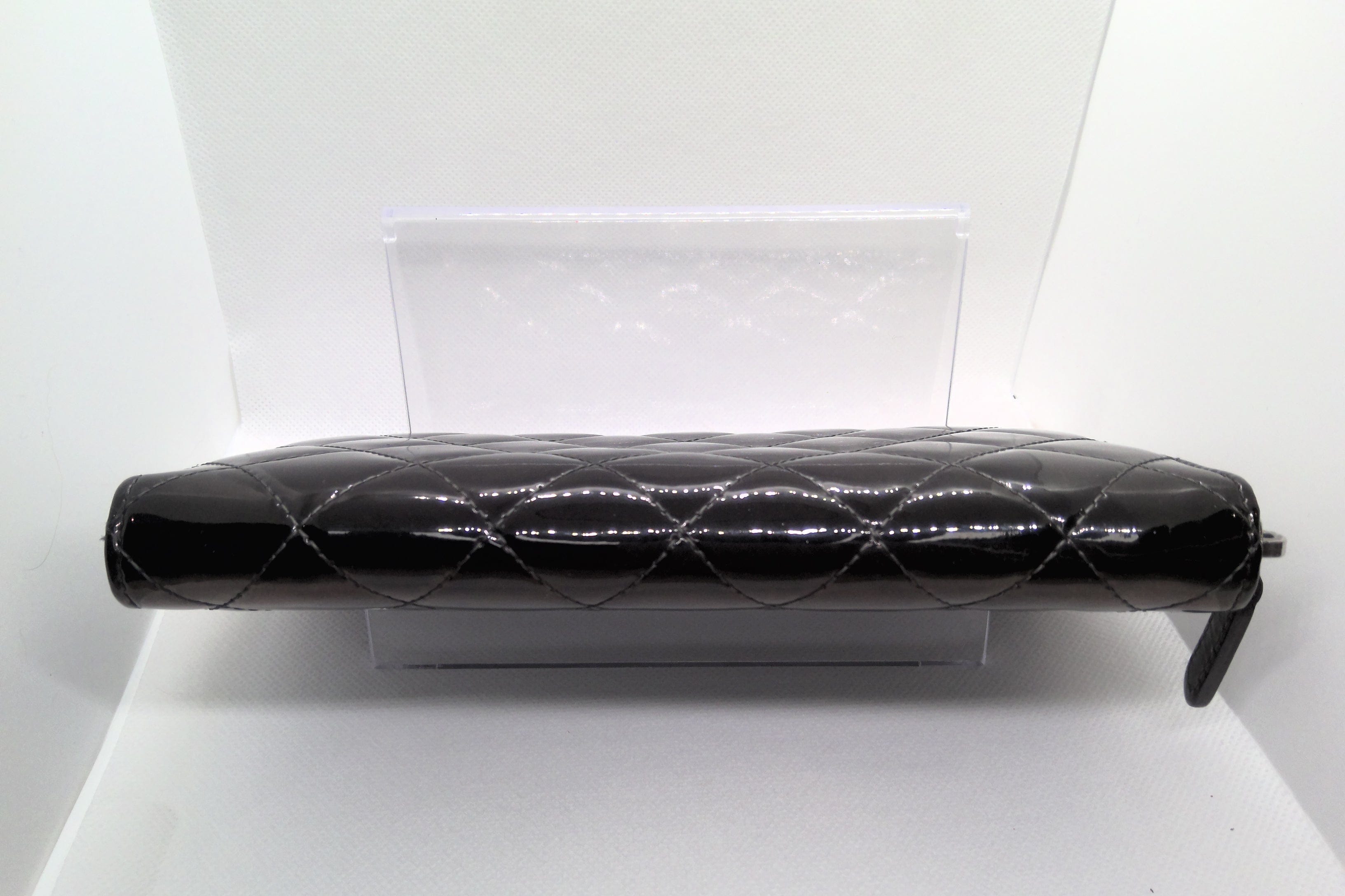 Black quilted handbag on a white stand with a white background