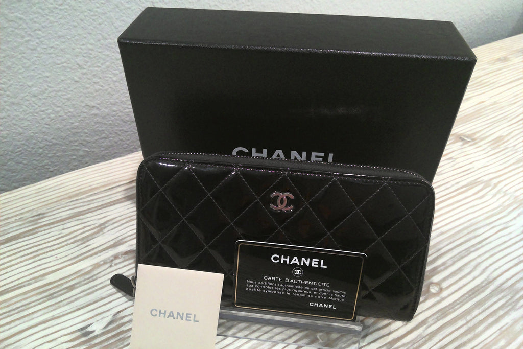 Black quilted Chanel wallet with box and card on a light wooden surface