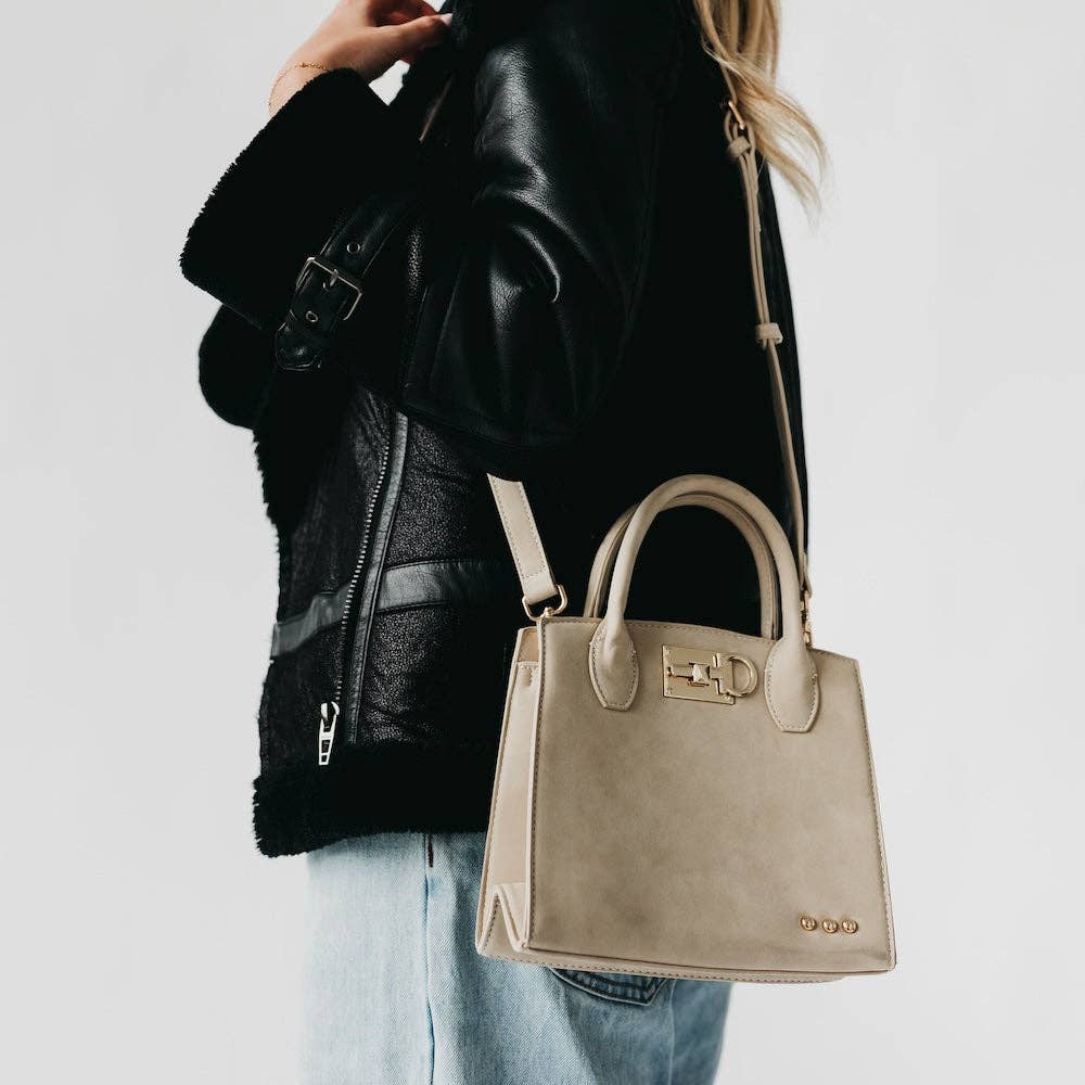 Person wearing a black leather jacket with a beige handbag on a light gray background
