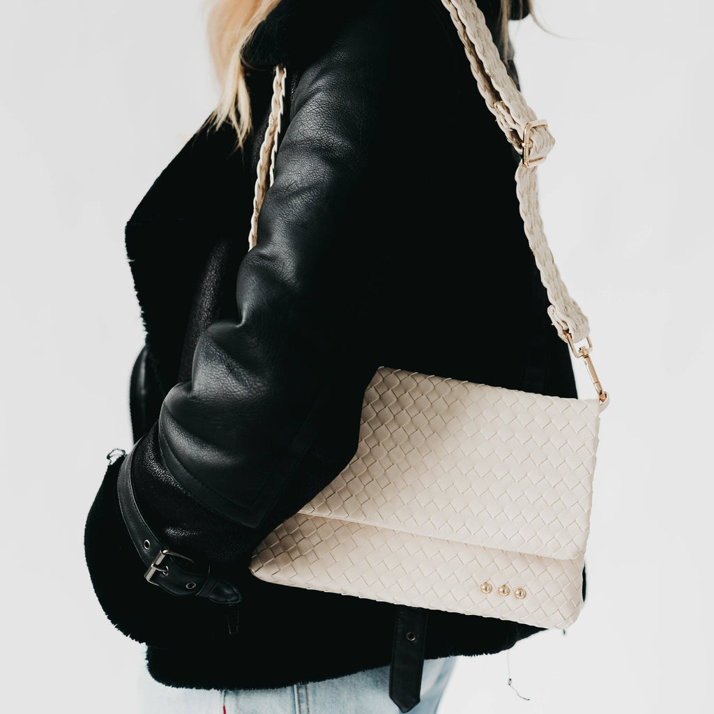 Beige handbag with braided handle worn over a black leather jacket on a light background