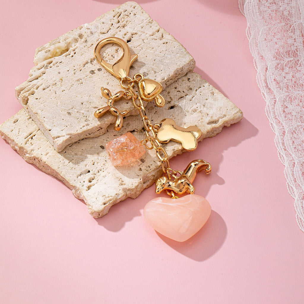 Gold keychain with pink heart and dog charms on a textured stone surface with a pink background