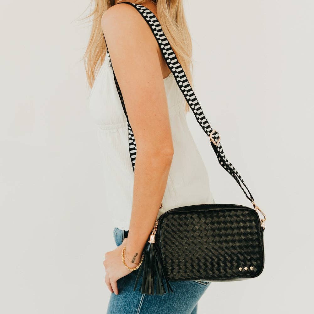 Person holding a black woven handbag with a striped strap against a white background
