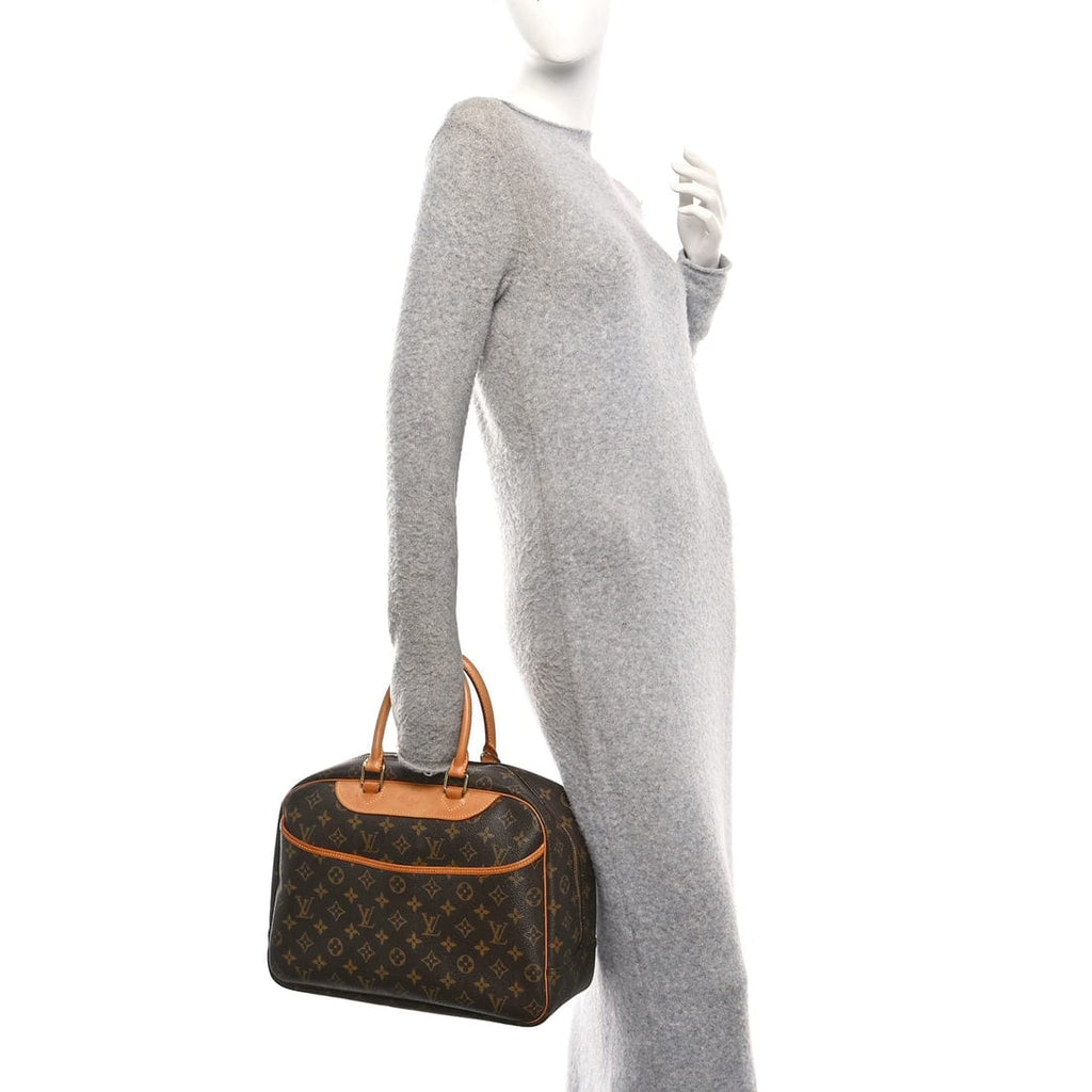 A Louis Vuitton monogram handbag with tan leather handles and trim, shown being carried by a headless mannequin wearing a light gray knit dress against a plain white background.