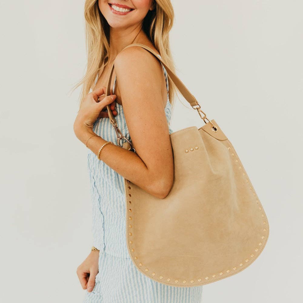 Woman holding a beige handbag against a plain background