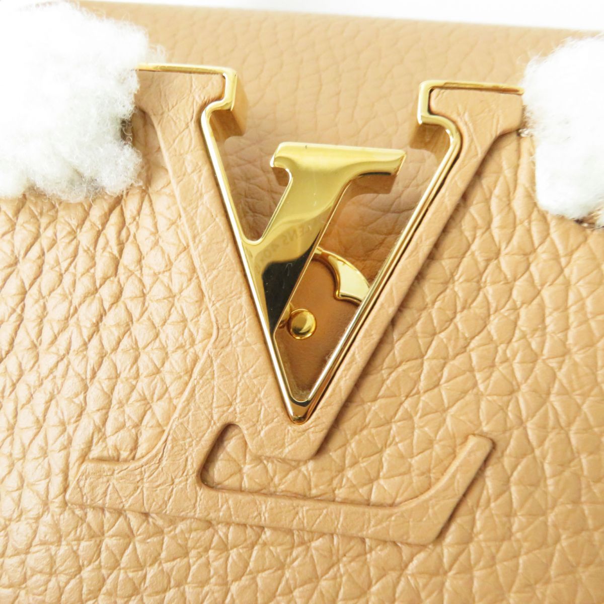 Close-up of a beige textured surface with a gold 'V' logo and white fluffy elements.