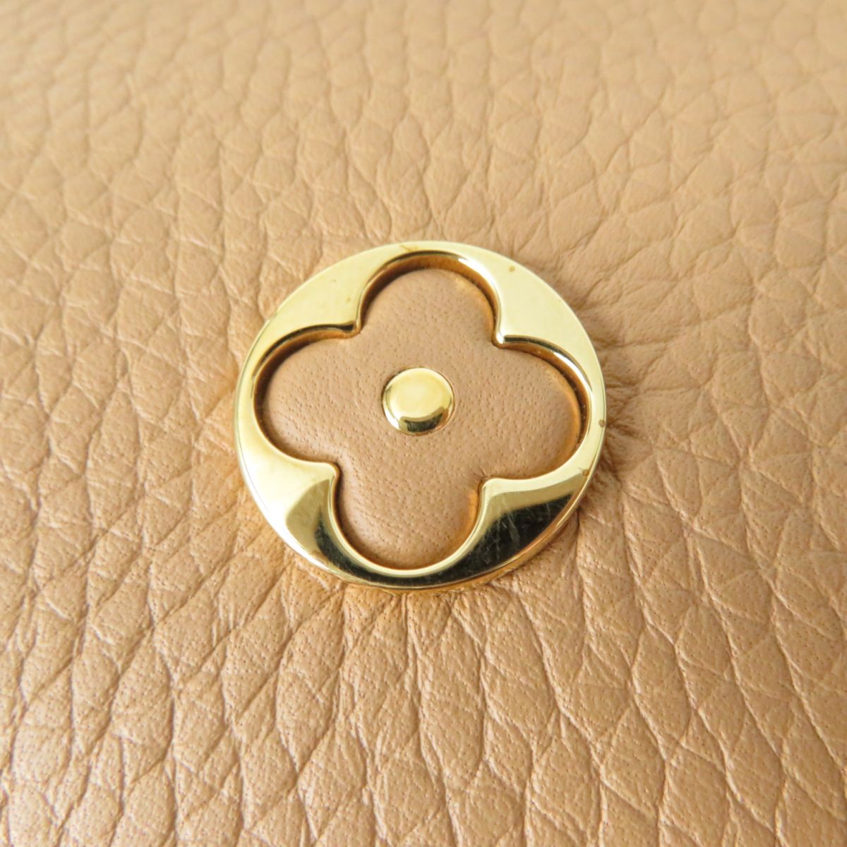 Close-up of a gold floral design button on beige leather.