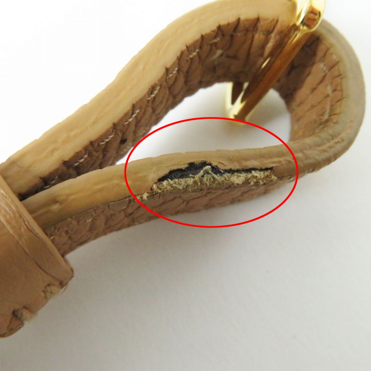 Close-up of a brown leather strap with a gold buckle, showing a worn area circled in red.