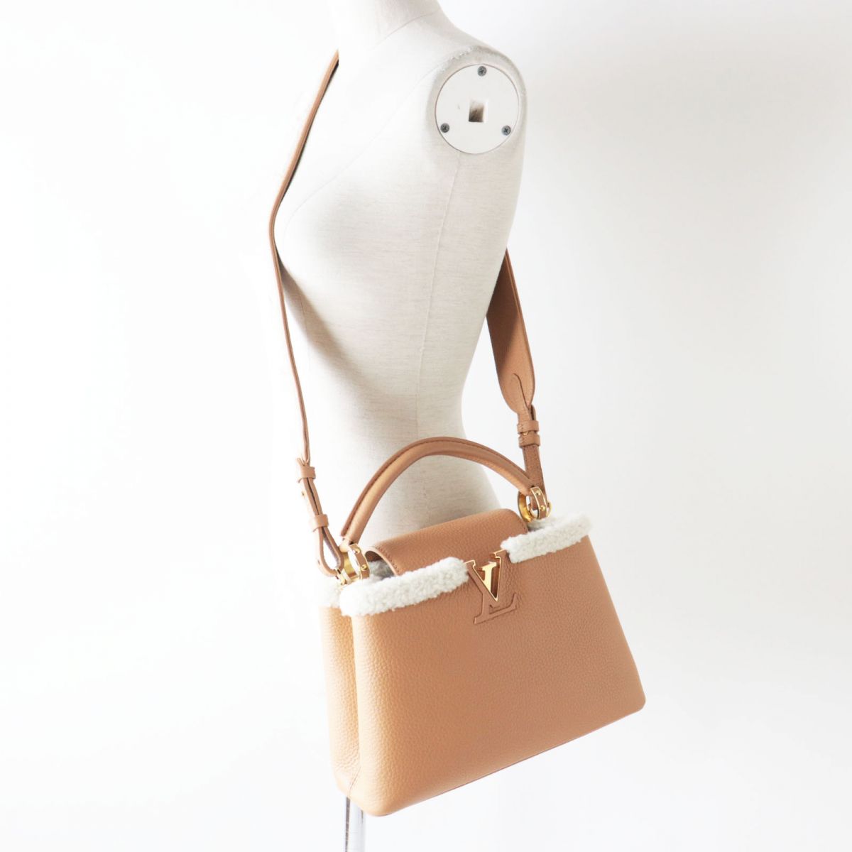 Tan handbag with white fur trim on a mannequin against a white background