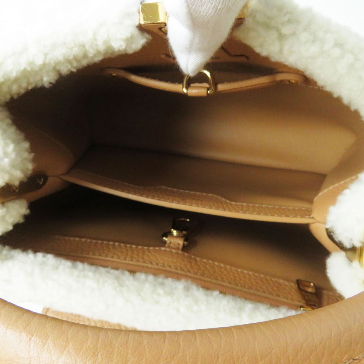 Close-up of a brown leather handbag with gold hardware on a white fluffy background