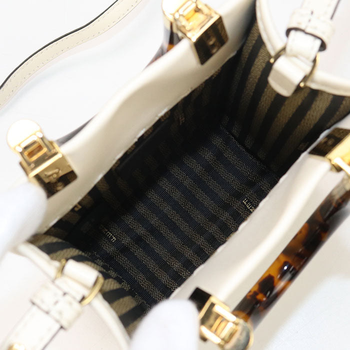 Close-up of a white handbag with gold accents and black interior lining.