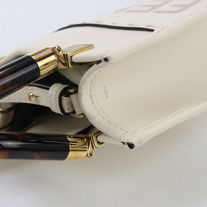 Close-up of a white handbag with gold and tortoiseshell accents on a light gray background