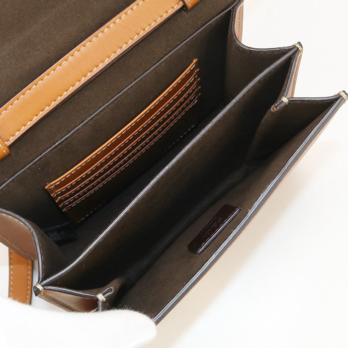 Close-up of a brown leather handbag with tan interior and strap on a white background
