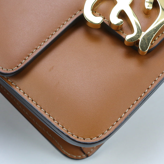 Close-up of a brown leather handbag with a gold logo on a light gray background