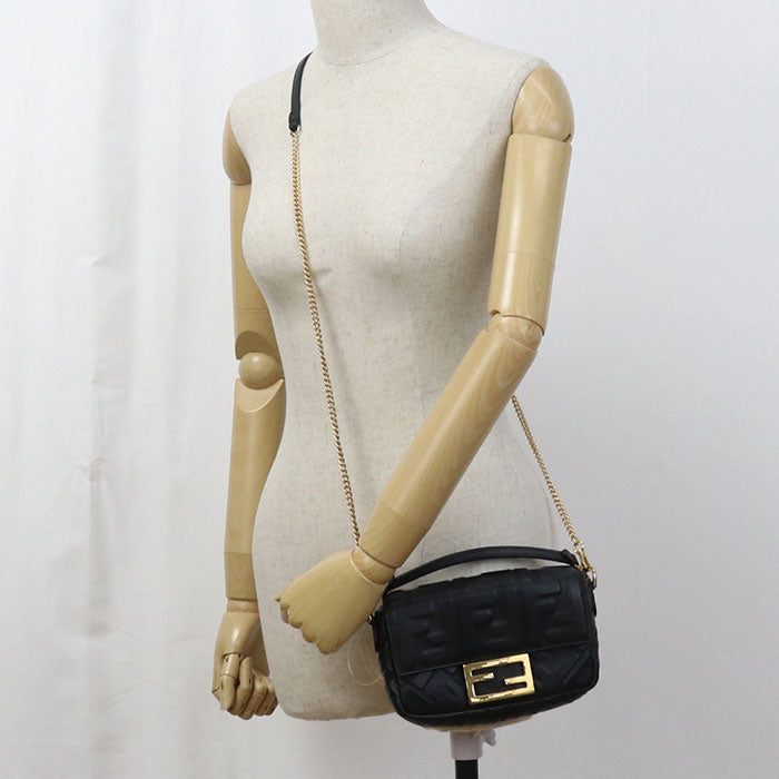 Black handbag with gold chain strap on a mannequin against a white background