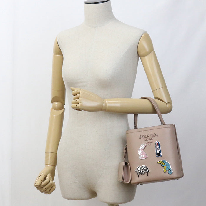 Mannequin holding a Prada handbag with decorative pins on a white background